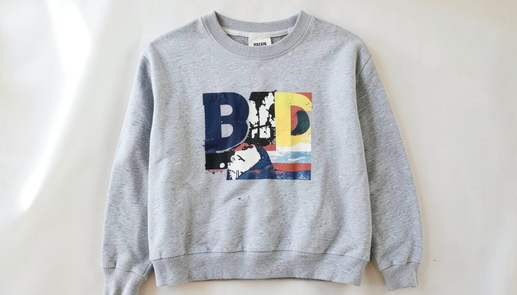 A grey marl sweatshirt with a bold chest print, shown in soft natural light