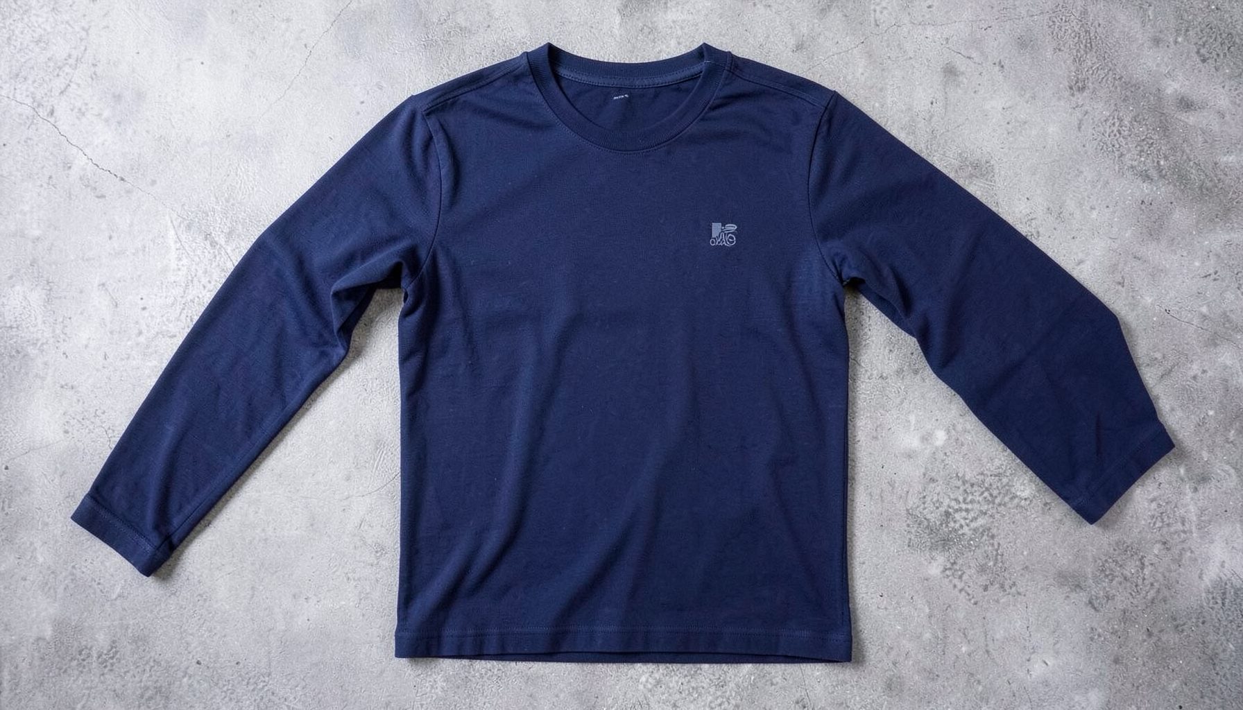 A navy blue long-sleeve shirt with a subtle logo detail, laid flat on a textured surface