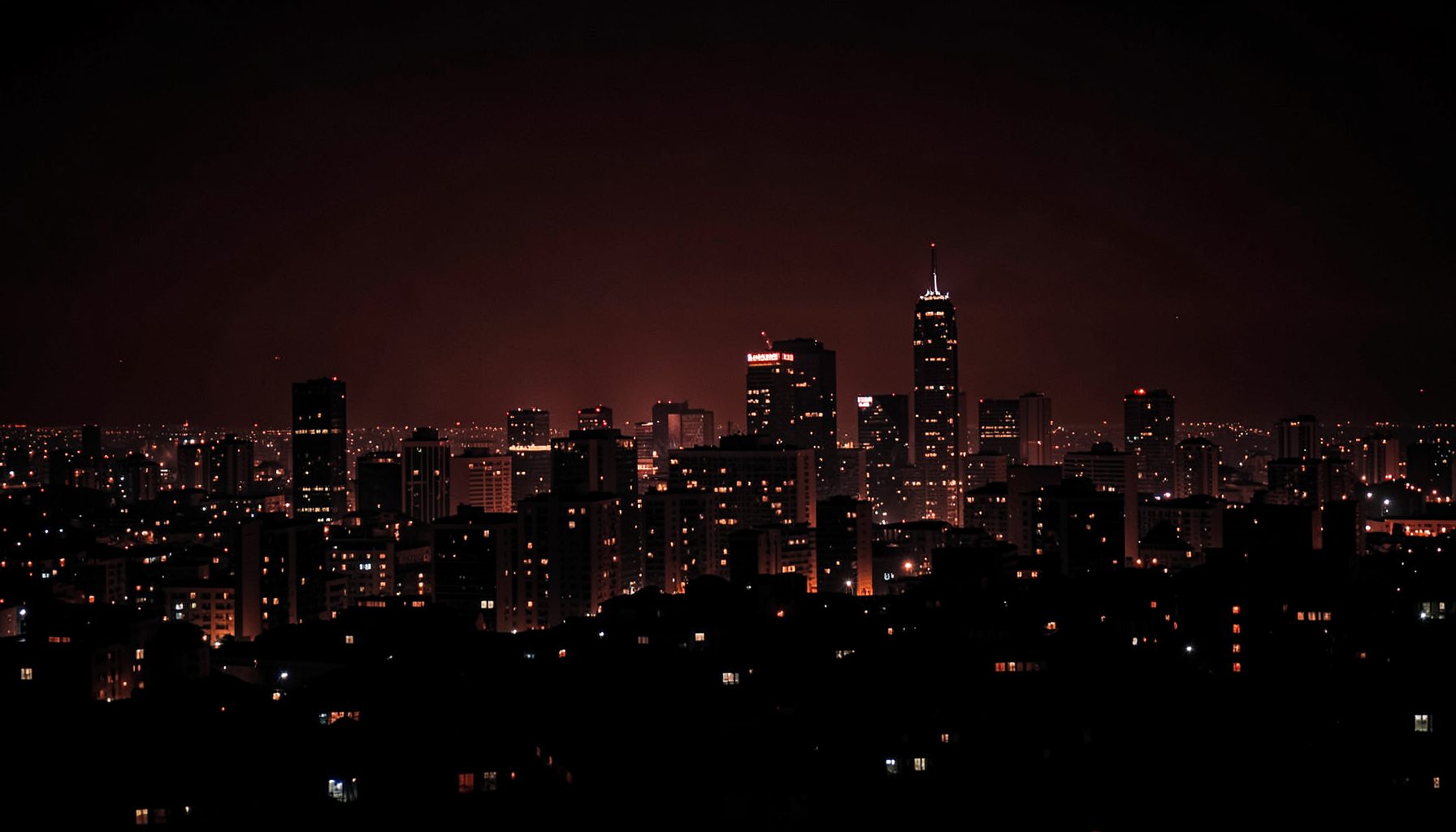 Dark moody photograph of a city skyline at night in deep red and charcoal tones, evoking a bold and creative atmosphere